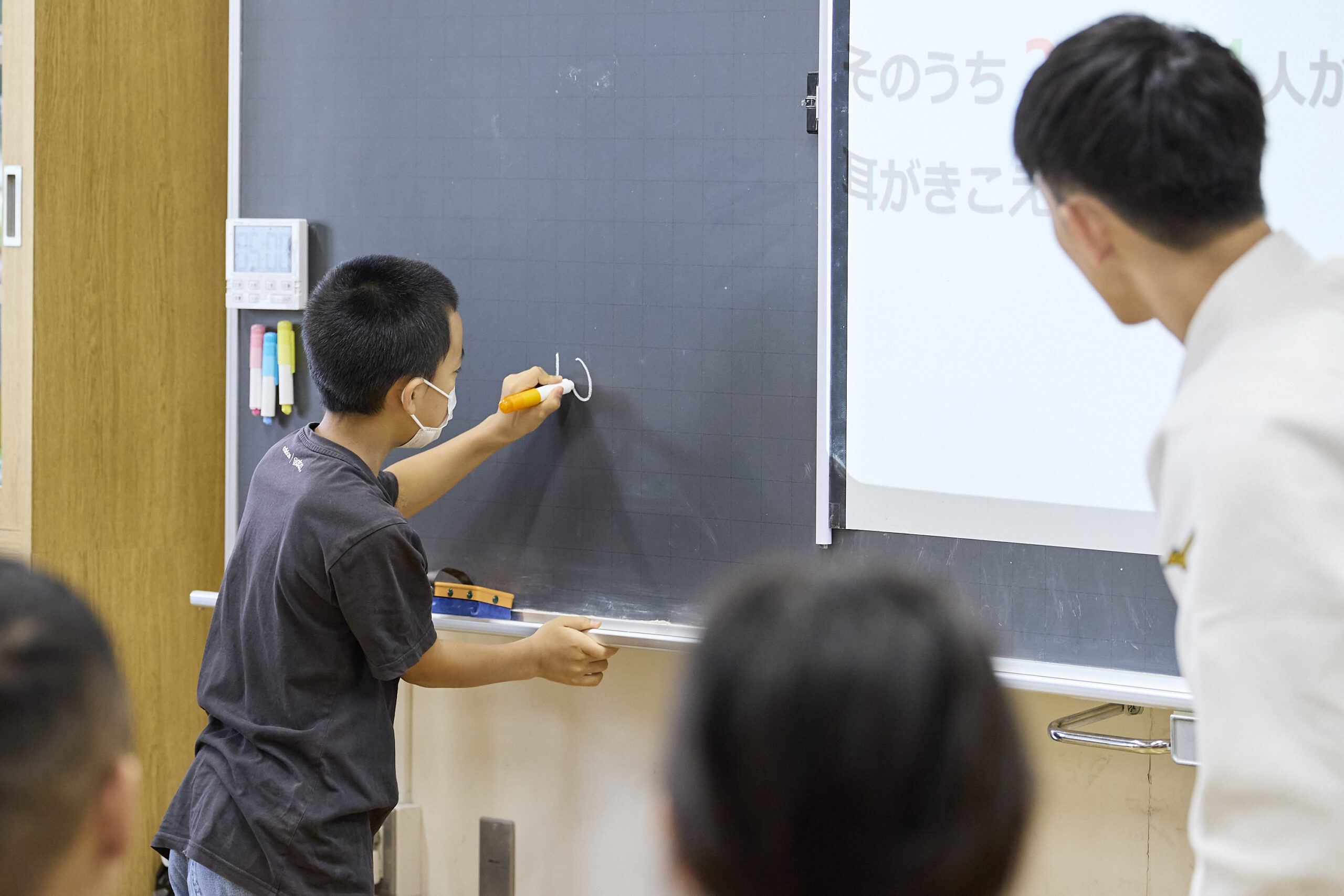 黒板に何かを書いている児童とそれを覗き込んでいる佐藤選手の写真