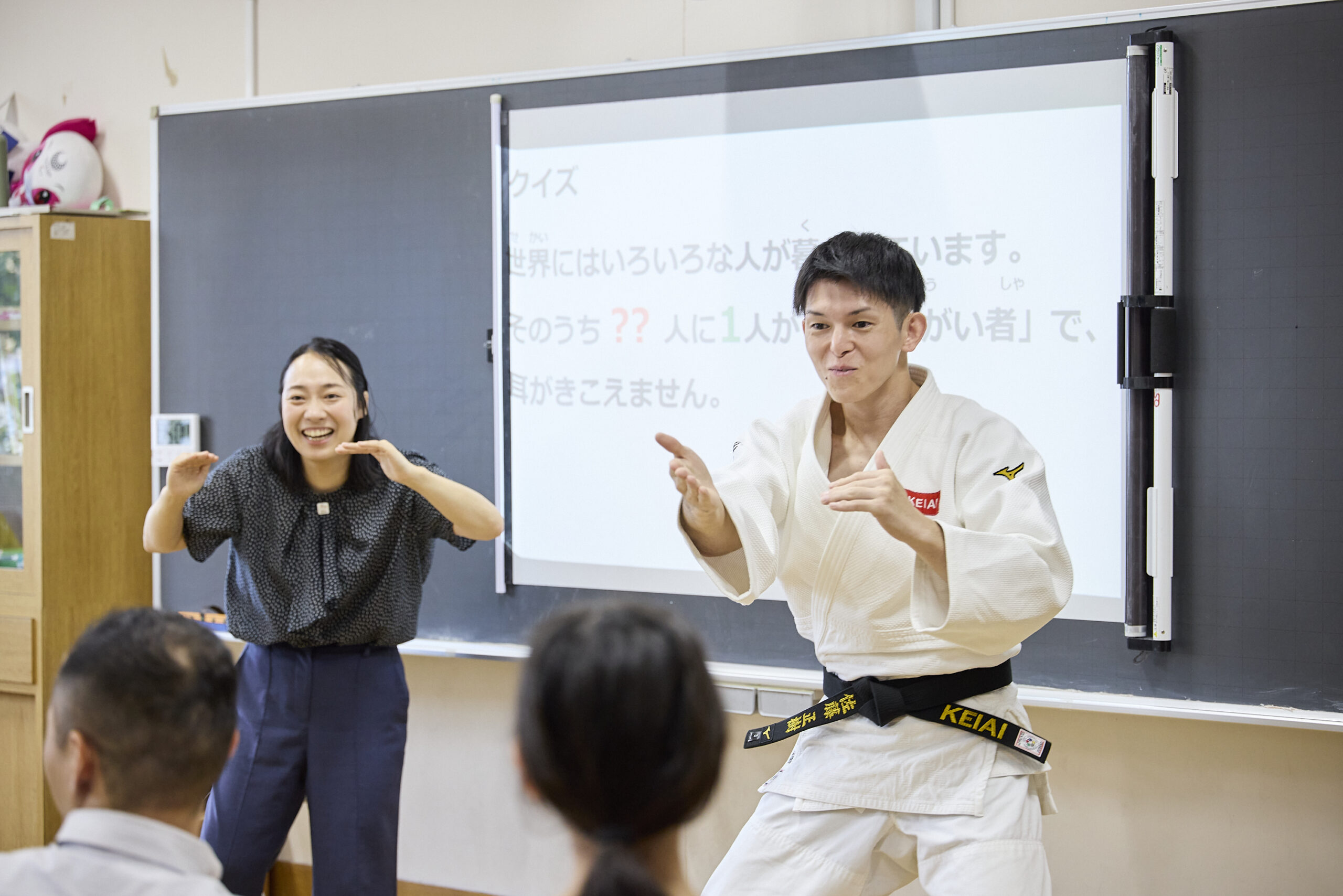 ジェスチャーで子供たちに何かを訴えている川俣さんと佐藤選手の写真
