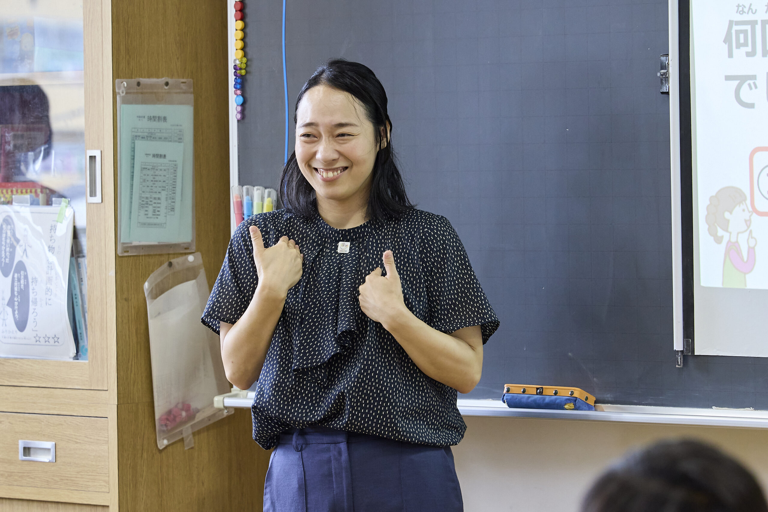 両手で自分を指しながら児童に笑顔を向けている川俣さんの写真
