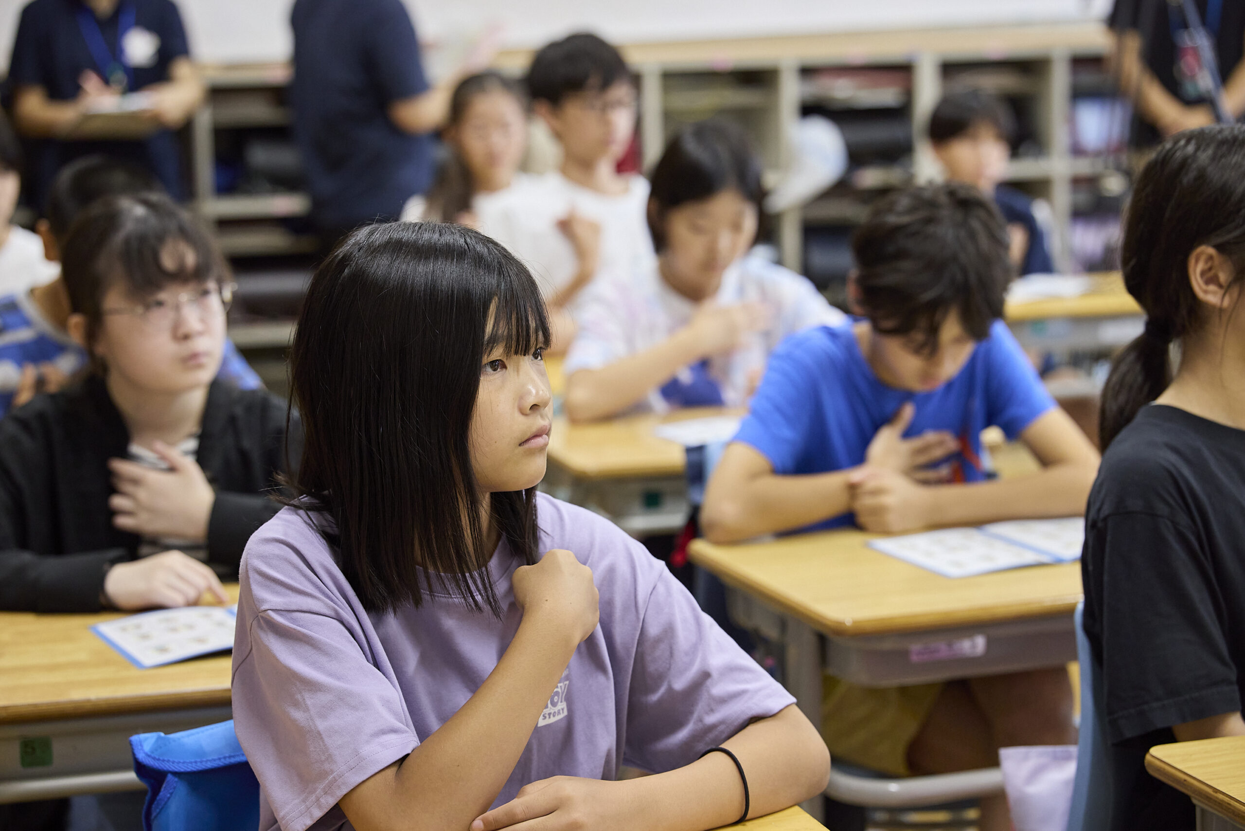 右手を左肩に置き真剣に登壇者の話を聞いている児童の写真