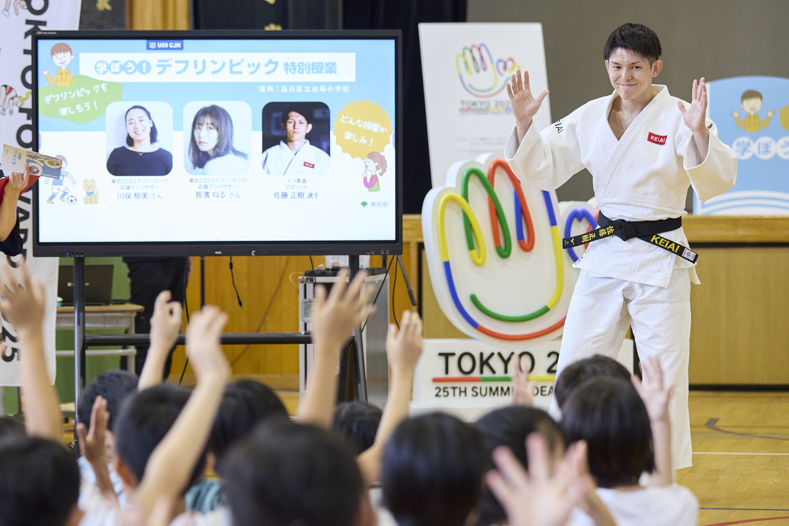 両手を肩のあたりまで上げて登場した佐藤選手と拍手の手話をしている児童の写真