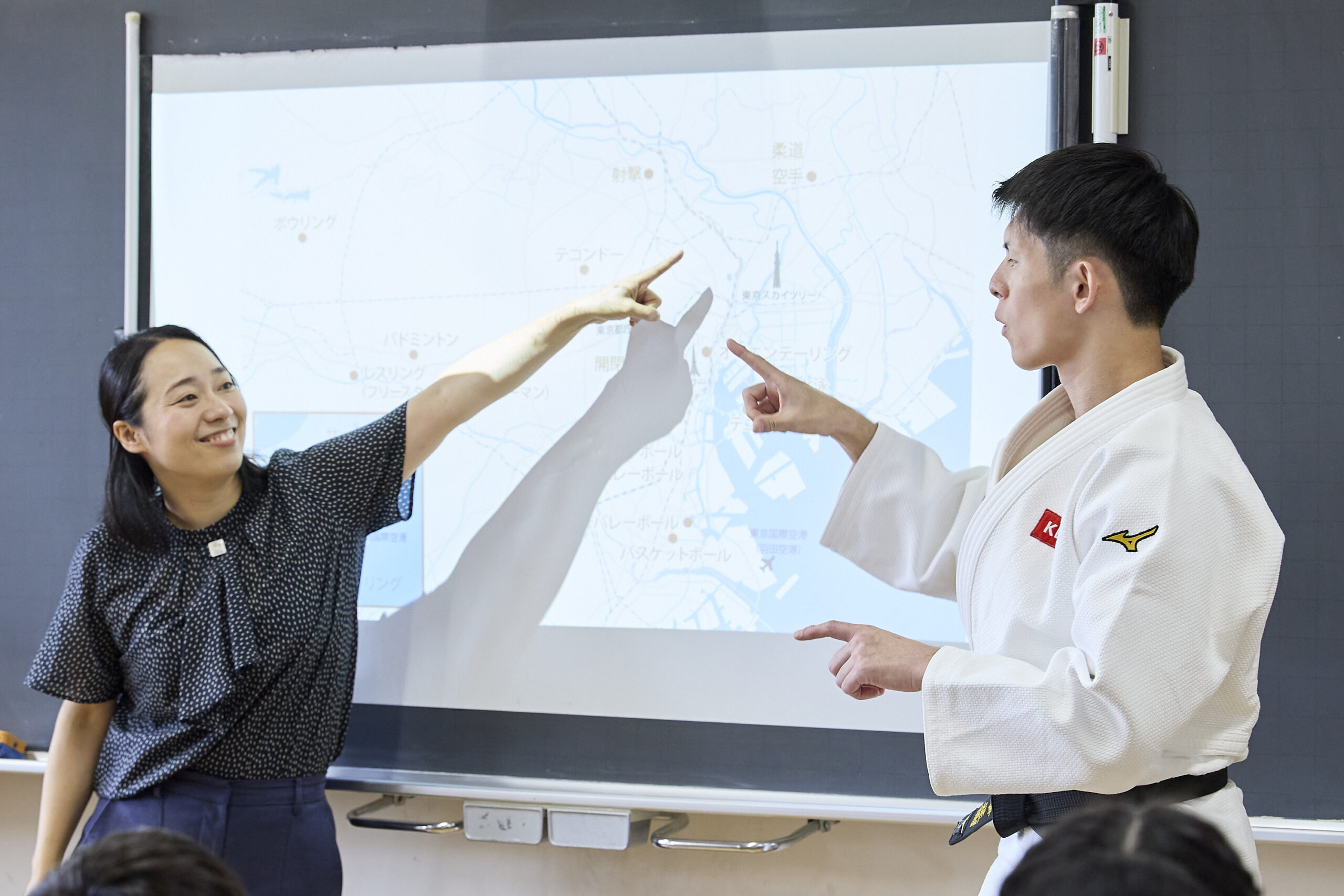 地図が表示されているスクリーンを指さしている川俣さんと佐藤選手の写真