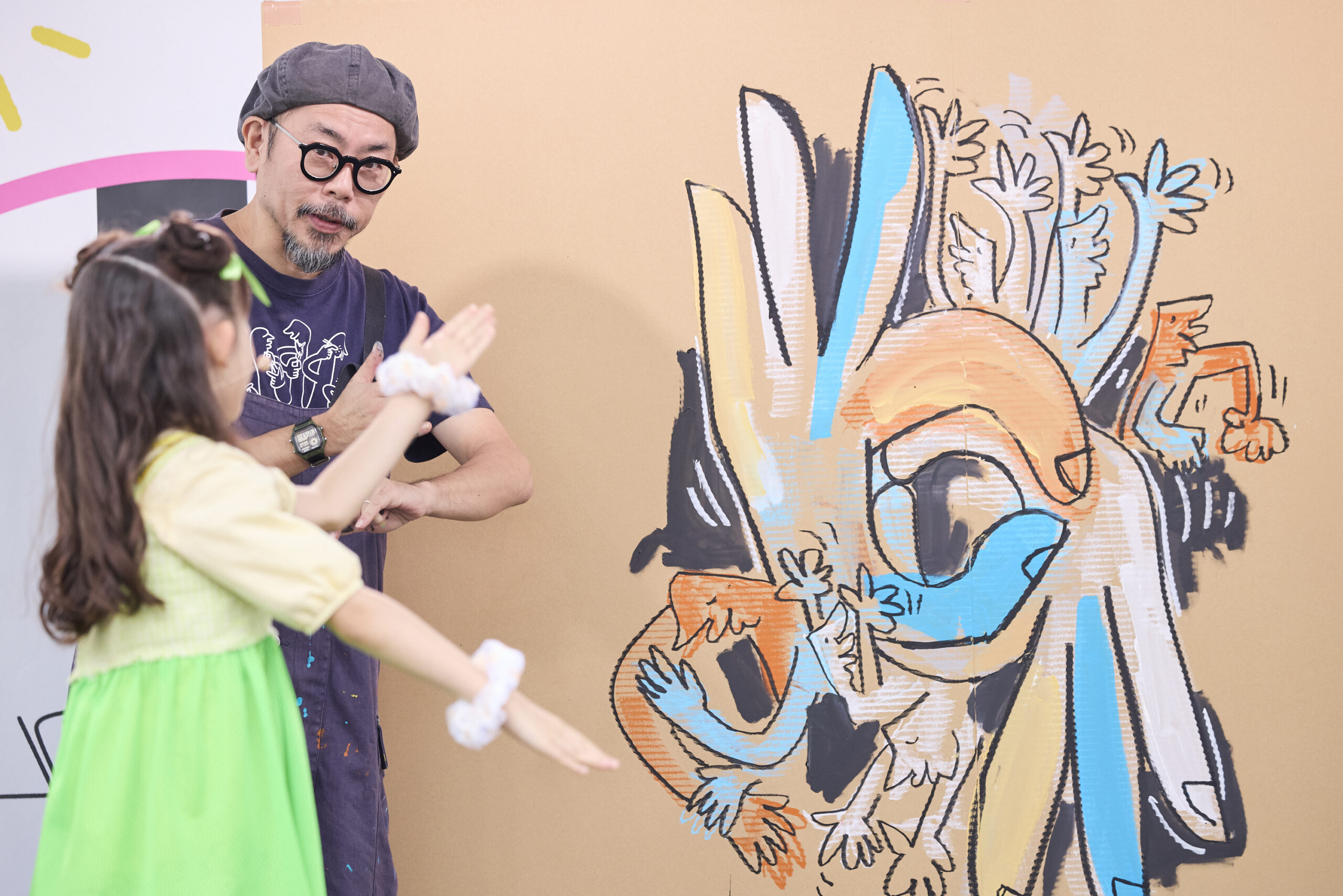 描かれた壁の前で門さんとミドリーズの女の子がありがとうの手話をしている写真