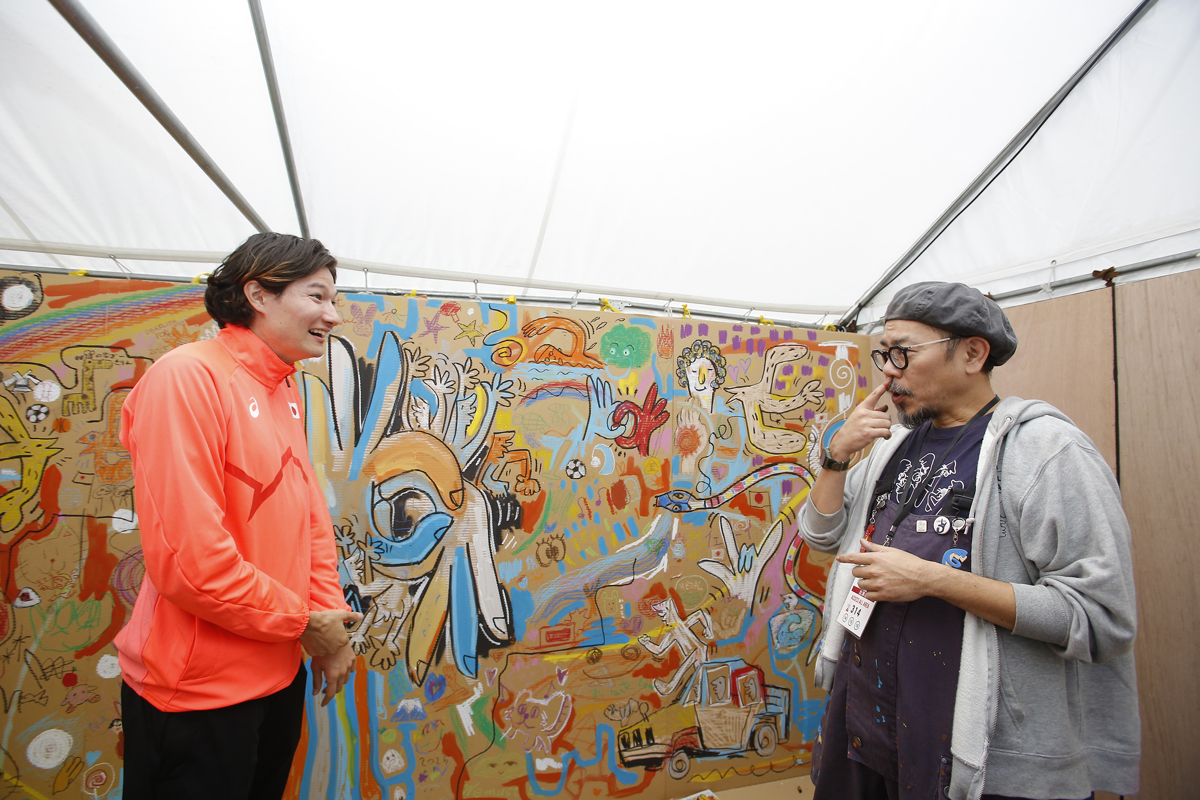 絵が描かれた壁の前で山田選手と門さんが手話で話しをしている写真
