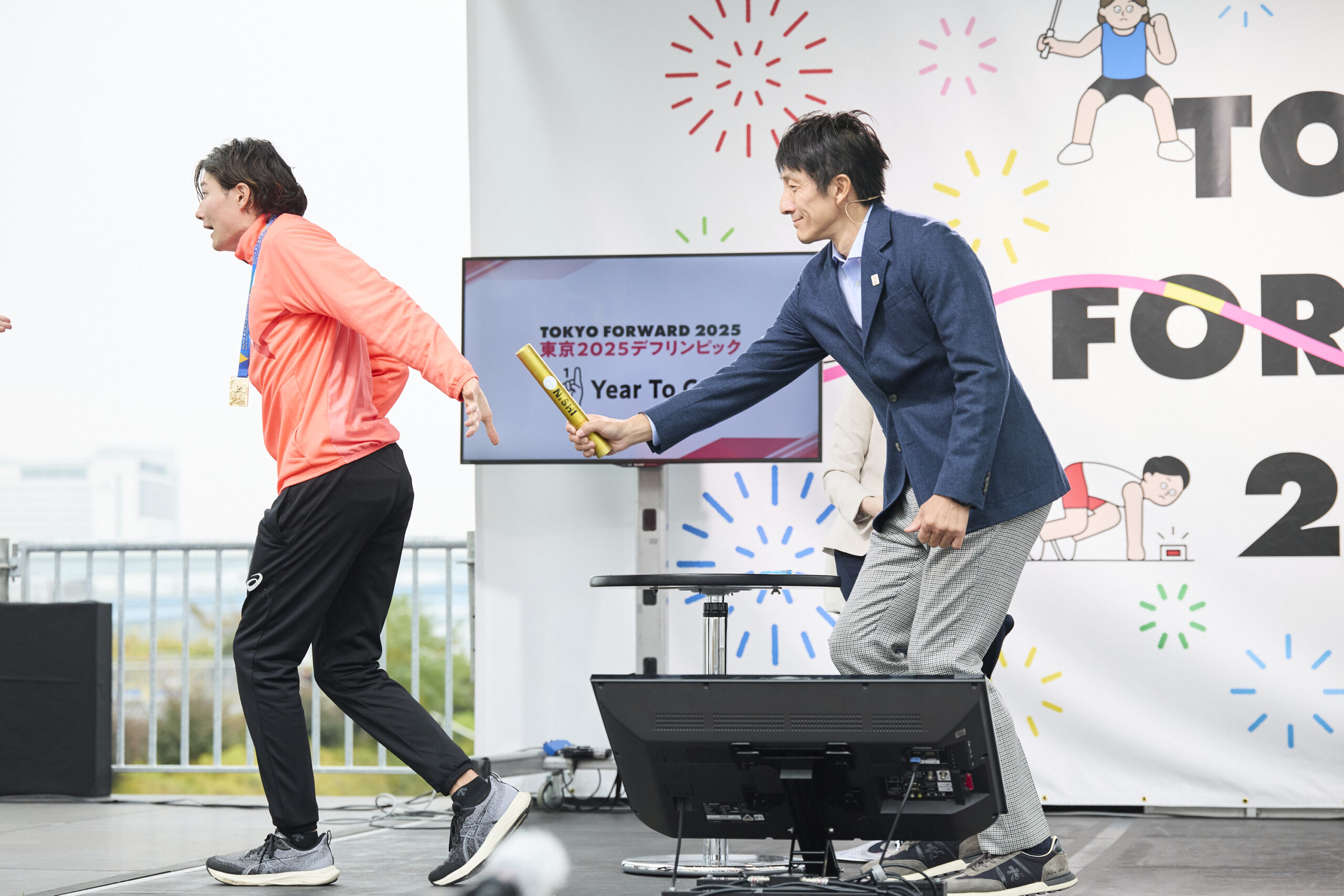 左手を後ろにしバトンを受け取ろうとしている山田選手とバトンを渡そうとしている朝原さんの写真