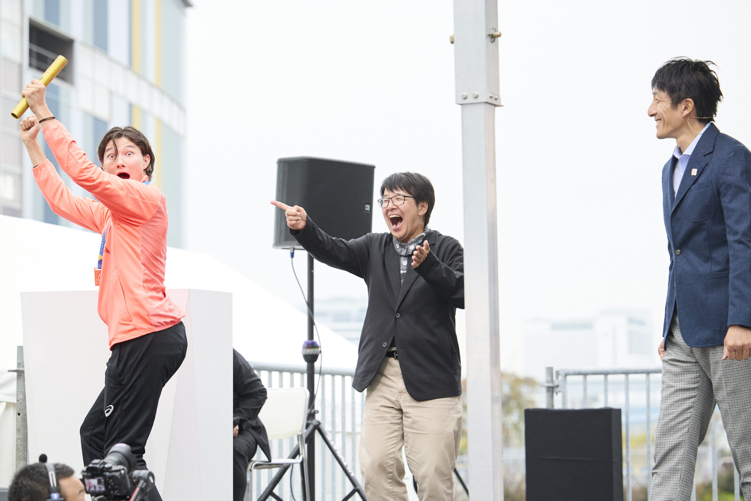 バトンを受け取って喜んでいる山田選手とMCと朝原さんの写真