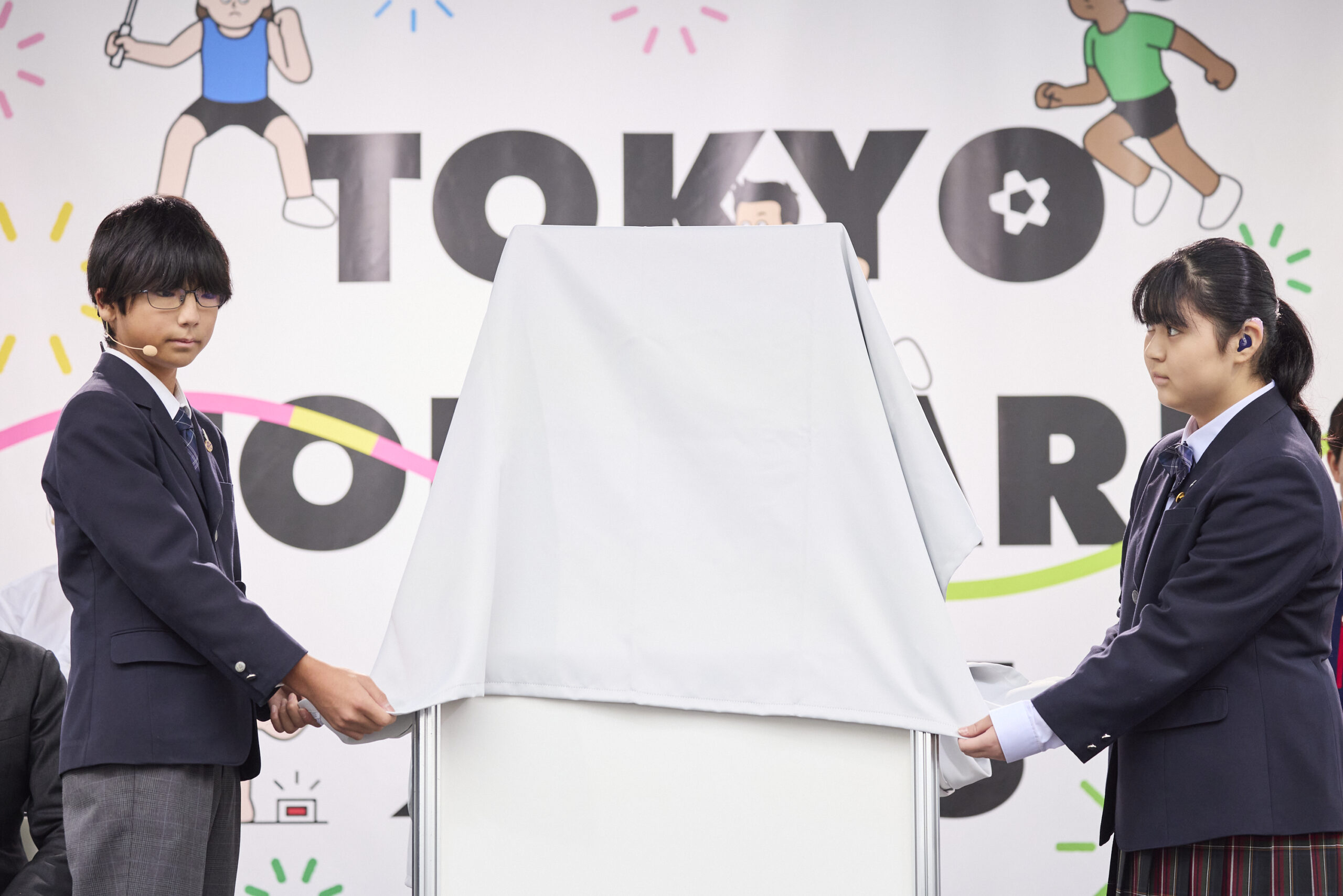 児童二人がメダルが入っているショーケースにかかっているベールを取ろうとしている写真